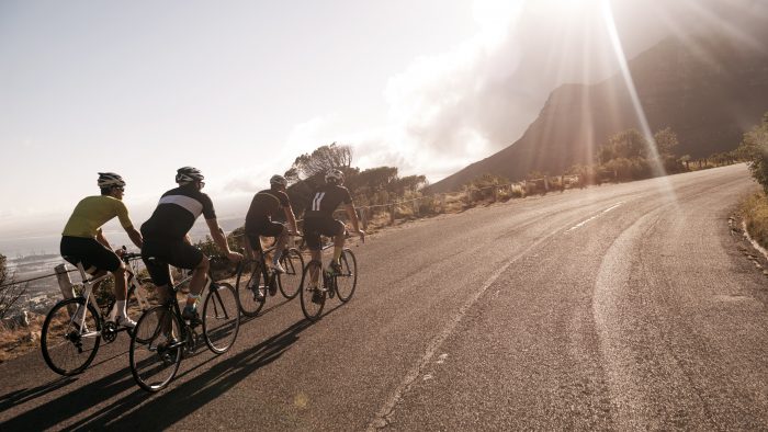 A group of cyclists racing up a mountain facing a low sun.
