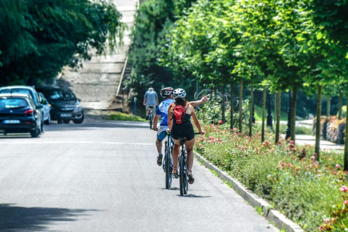 People cycling on a road beside bright trees and flowers.