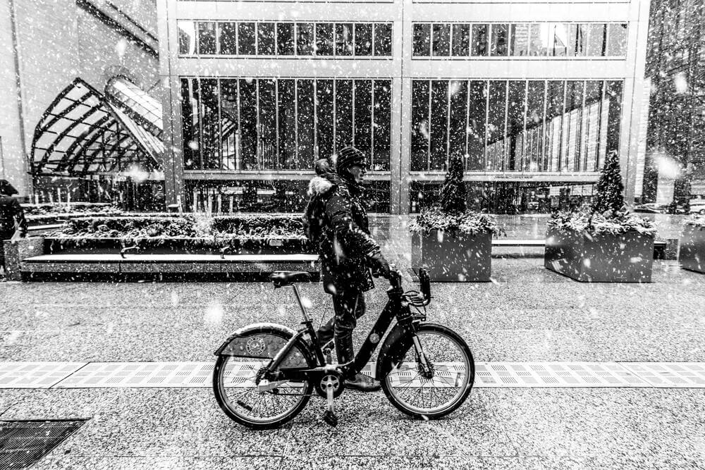 A man riding his bike in the snow and dim light
